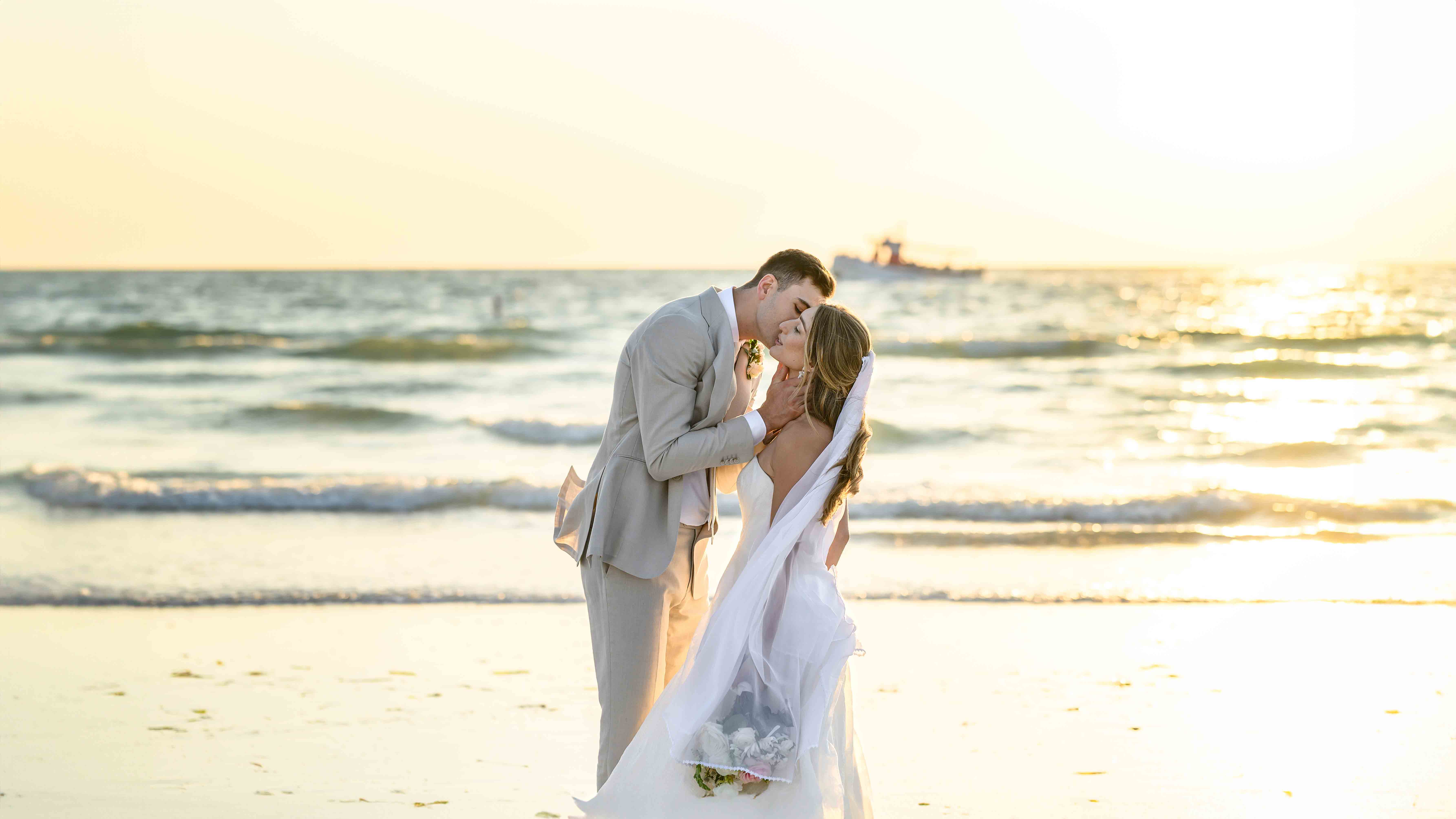 Husband kissing his bride on the cheeck on the beach during sunset