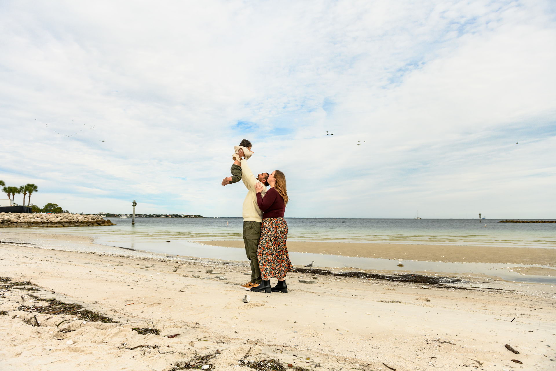 Photo of a mother and father on a beach holding their child